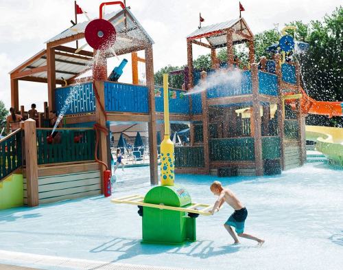 A child plays at a colorful water park with slides and splash features on a sunny day. Water sprays around him.