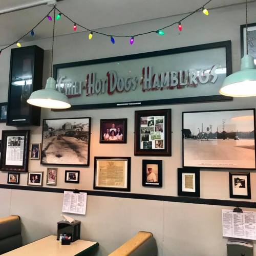 A diner wall featuring a vintage sign, framed photos, and newspaper clippings, with colorful string lights above.