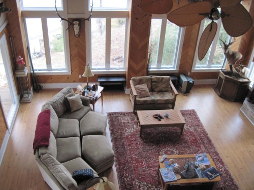 A spacious living room with large windows, a sectional sofa, armchairs, a coffee table, and rustic decor.