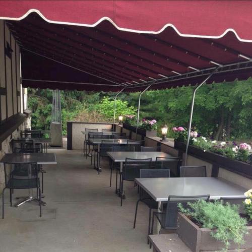 Outdoor dining area with tables and chairs under a red awning, surrounded by greenery.