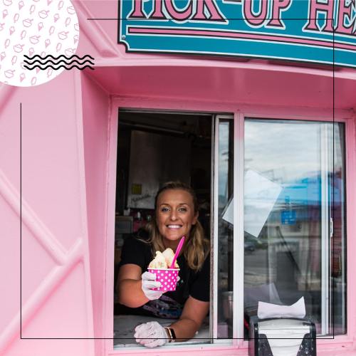 A smiling woman serves ice cream from a pink food truck window, holding a colorful cup with a spoon.