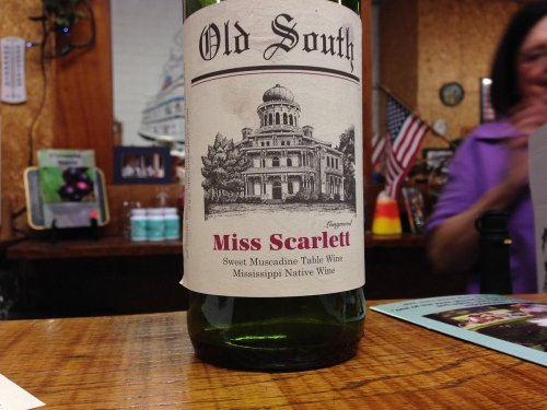 A bottle of "Old South Miss Scarlett" sweet muscadine table wine with a historic building illustration on the label.