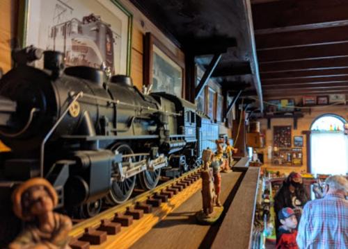 A model steam train displayed on a shelf, surrounded by figurines and framed pictures in a cozy room.