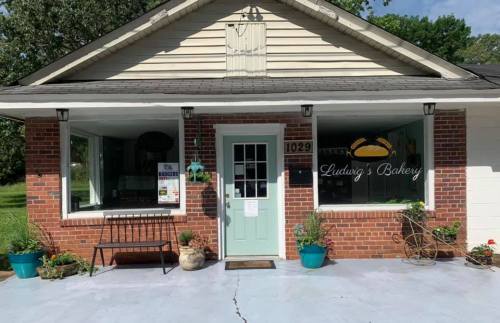 A charming bakery with a brick exterior, green door, and potted plants outside, featuring large windows.