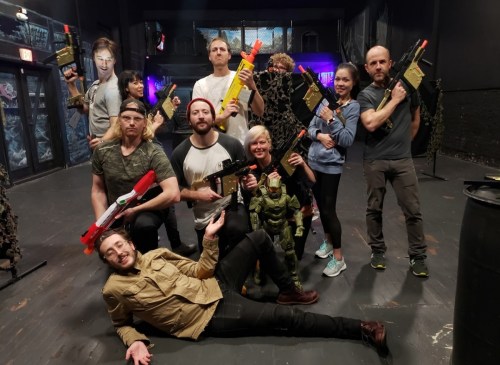 A group of people posing with toy guns in a dimly lit indoor space, some wearing casual clothing and playful expressions.