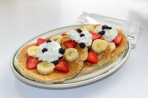 A plate of pancakes topped with strawberries, bananas, blueberries, and whipped cream.