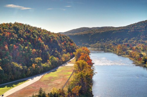 Scenic view of a river winding through colorful autumn foliage and rolling hills under a clear blue sky.