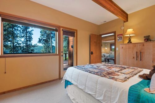 Cozy bedroom with a large window showcasing a forest view, featuring a bed with a patterned blanket and wooden accents.