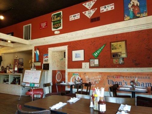 Interior of a cozy restaurant with a red wall covered in signatures, vintage signs, and wooden tables set for dining.