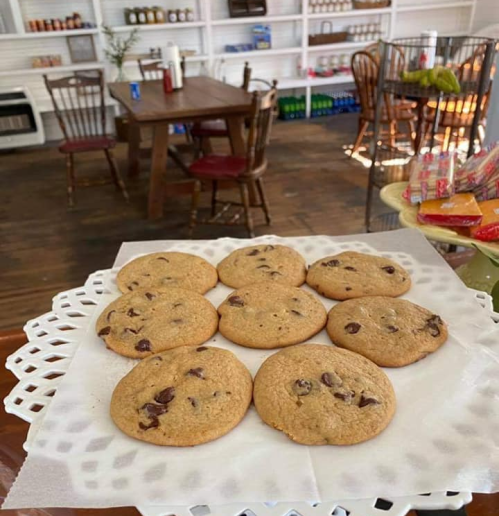 A plate of freshly baked chocolate chip cookies on a lace doily, with a cozy kitchen setting in the background.