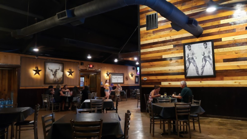 Interior of a rustic restaurant with wooden walls, tables, and patrons dining. Artwork and star decorations are visible.