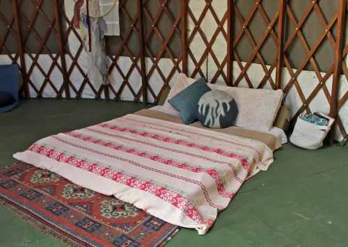 Cozy interior of a yurt featuring a bed with patterned blankets and pillows, and a decorative rug on the floor.