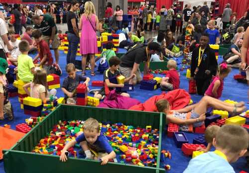 A vibrant scene of children playing with colorful building blocks in a busy indoor space filled with families.