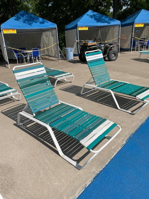 Two green and white lounge chairs are positioned near a pool area, with tents and equipment in the background.