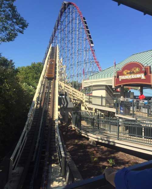 A wooden roller coaster, Thunderhawk, ascends steeply against a clear blue sky.