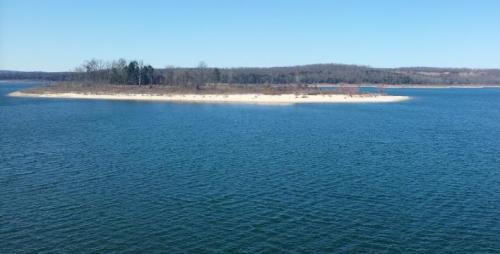 A serene view of a small sandy island surrounded by calm blue water under a clear sky.