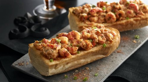 Two toasted bread rolls topped with a savory shrimp mixture, garnished with green onions, on a dark slate plate.