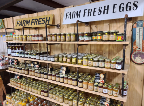 Shelves filled with jars of preserves and a sign for "Farm Fresh Eggs" in a rustic market setting.