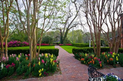 A picturesque garden path lined with colorful flowers and greenery, leading through manicured hedges and trees.