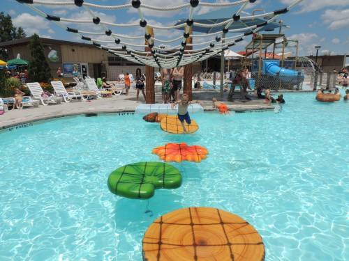 A pool scene with colorful floating obstacles and people enjoying the water under a sunny sky.
