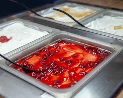 A metal tray filled with bright red cherry topping, surrounded by other dessert options in metal containers.