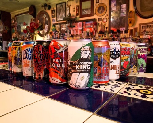 A colorful display of various craft beer cans arranged on a tiled bar counter.
