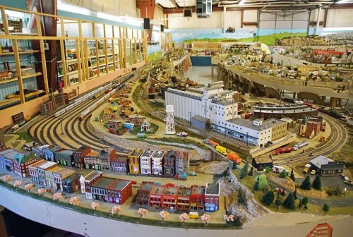 A detailed model train layout featuring tracks, buildings, and miniature landscapes in a spacious indoor setting.