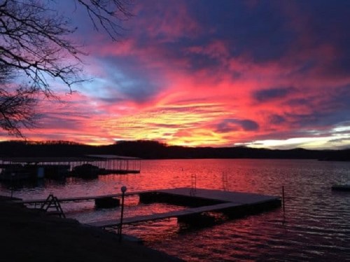 A vibrant sunset over a lake, with colorful clouds reflecting on the water and a dock in the foreground.