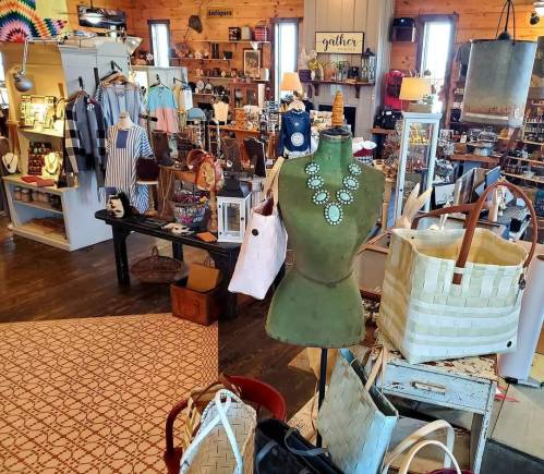 A cozy shop interior filled with vintage items, clothing, and accessories, featuring a green mannequin and various bags.