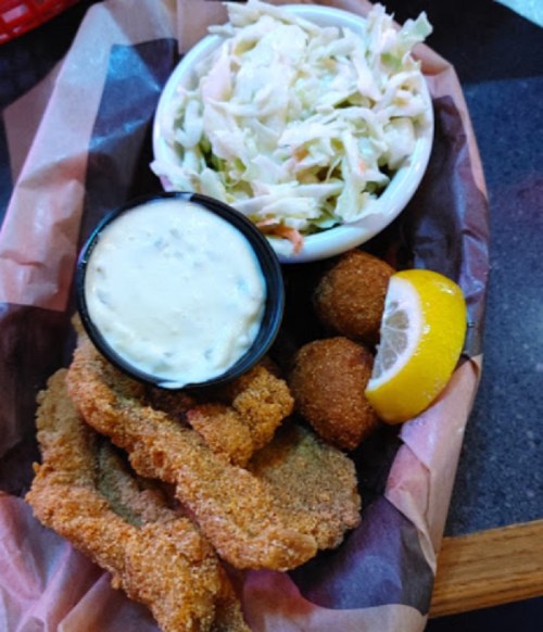 A plate of fried fish fillets, coleslaw, hushpuppies, a lemon wedge, and a small cup of tartar sauce.