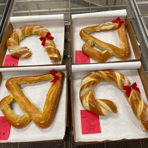 Four pretzels shaped like letters and symbols, each adorned with a red bow on a display tray.