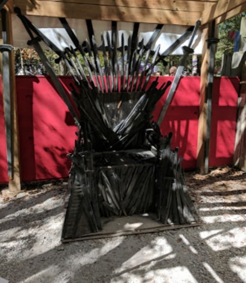 A throne made of swords, set in a shaded outdoor area with a red backdrop and gravel ground.