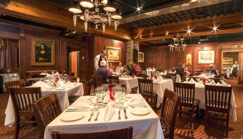 Elegant restaurant interior with wooden decor, tables set with white linens, and diners enjoying their meals.