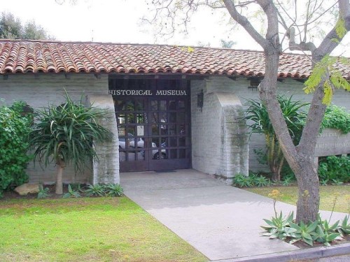 Entrance of a historical museum with a tiled roof, surrounded by greenery and a pathway.