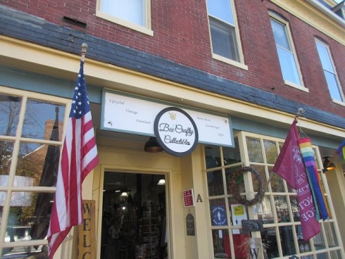 Storefront of "Bee & Sally's Collectibles" with an American flag and colorful banners hanging outside.