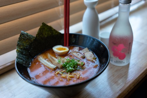 A bowl of ramen with sliced pork, egg, green onions, and seaweed, accompanied by a bottle of sake.