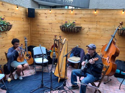 Two musicians perform in a cozy outdoor space, one with a violin and the other with a guitar, surrounded by plants.