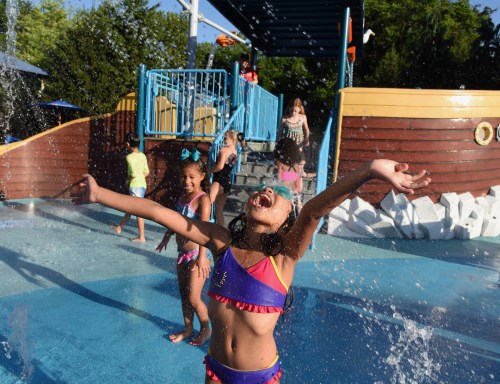 Children playing joyfully in a splash pad, water spraying around them on a sunny day.