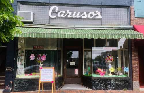 A charming candy shop with a green striped awning, colorful flower decorations, and a welcoming entrance.