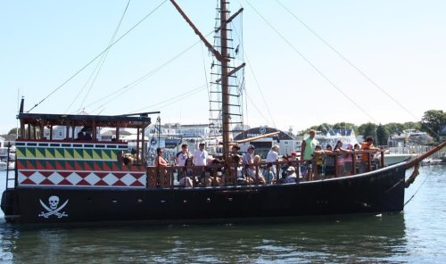 A colorful pirate ship with passengers on board, sailing in calm waters on a sunny day.