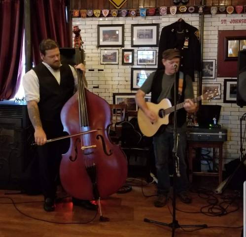 Two musicians perform in a cozy venue; one plays an acoustic guitar while the other plays a double bass.