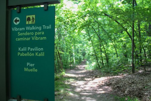 Sign for the Vibram Walking Trail, with directions to Kalil Pavilion and Pier, surrounded by lush green trees.