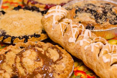 A variety of delicious pies and pastries, including fruit pies and a braided pastry drizzled with icing.