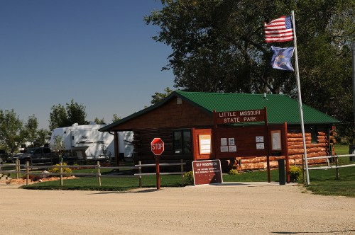 Entrance to Little Missouri State Park with a log cabin visitor center, flags, and a stop sign.