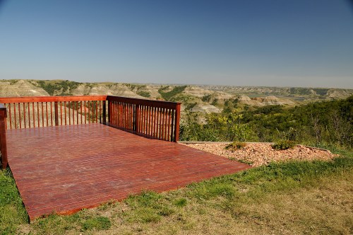 A wooden observation deck overlooks rolling hills and a clear blue sky in a scenic landscape.