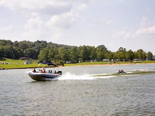 A boat with passengers speeds across a lake, while a person on a jet ski follows closely behind. Lush greenery in the background.