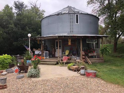 A rustic round metal building with a porch, surrounded by greenery and decorated with various vintage items and plants.