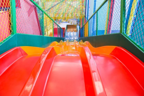 Colorful indoor slide with a smooth surface, leading down into a play area surrounded by netting and vibrant structures.