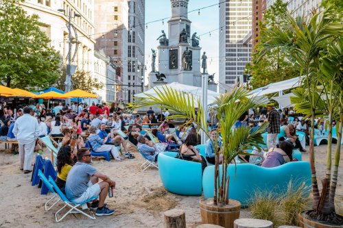 A lively outdoor gathering with people sitting in blue chairs, enjoying the atmosphere in a city park.
