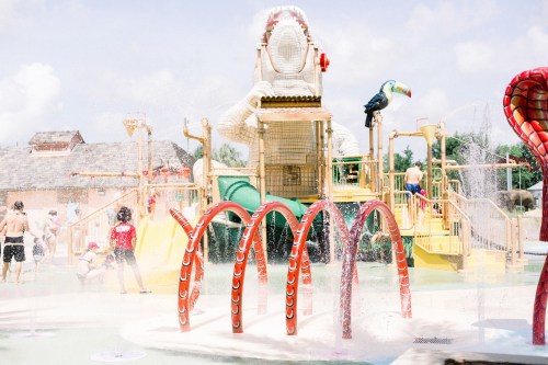 A colorful water playground with slides, spray features, and children playing in the water on a sunny day.